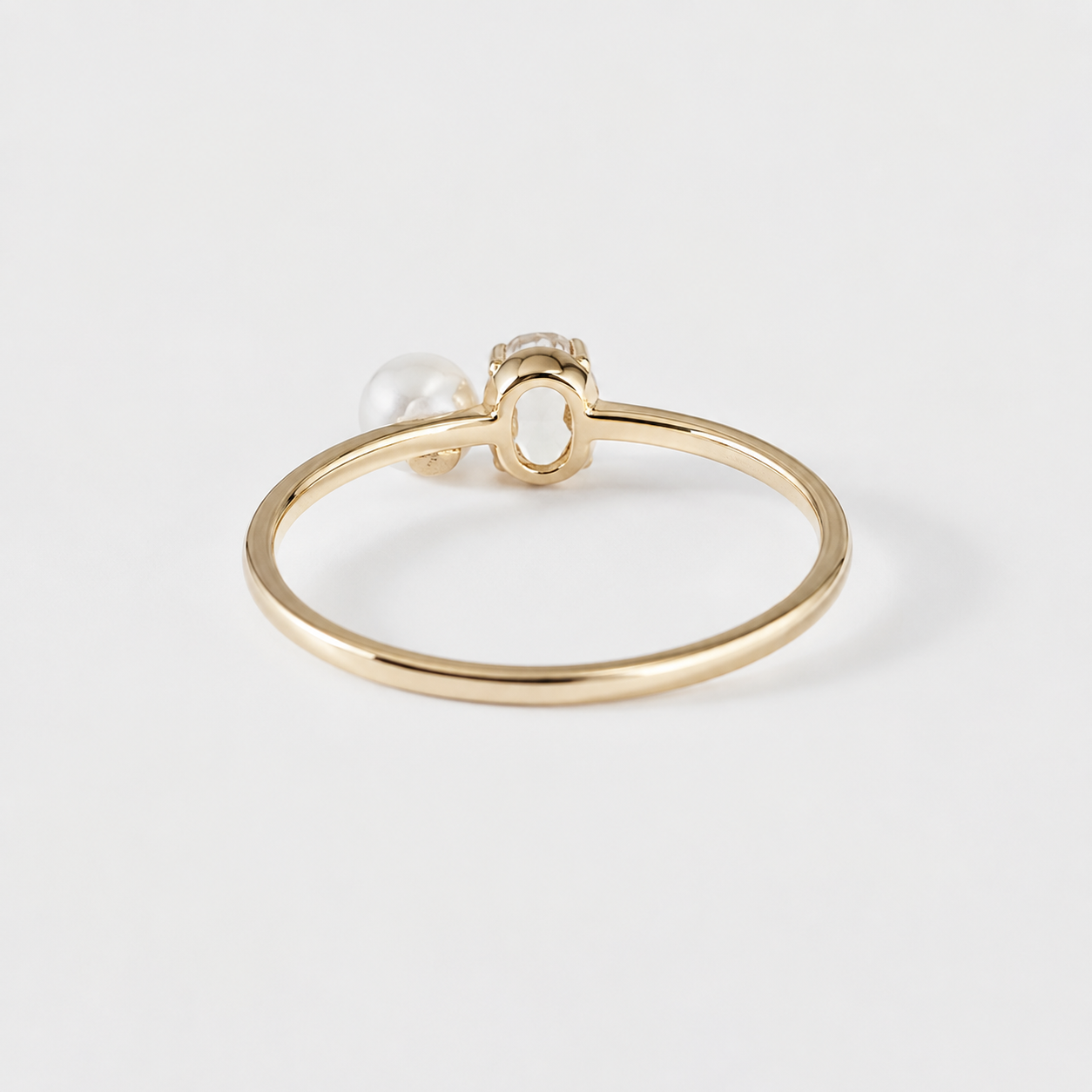 A delicate gold ring featuring a small white pearl and a tiny clear gemstone in a decorative setting, photographed on a clean white background.