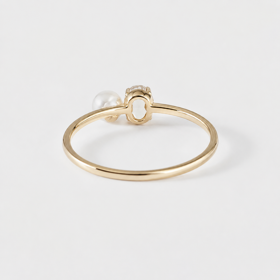 A delicate gold ring featuring a small white pearl and a tiny clear gemstone in a decorative setting, photographed on a clean white background.