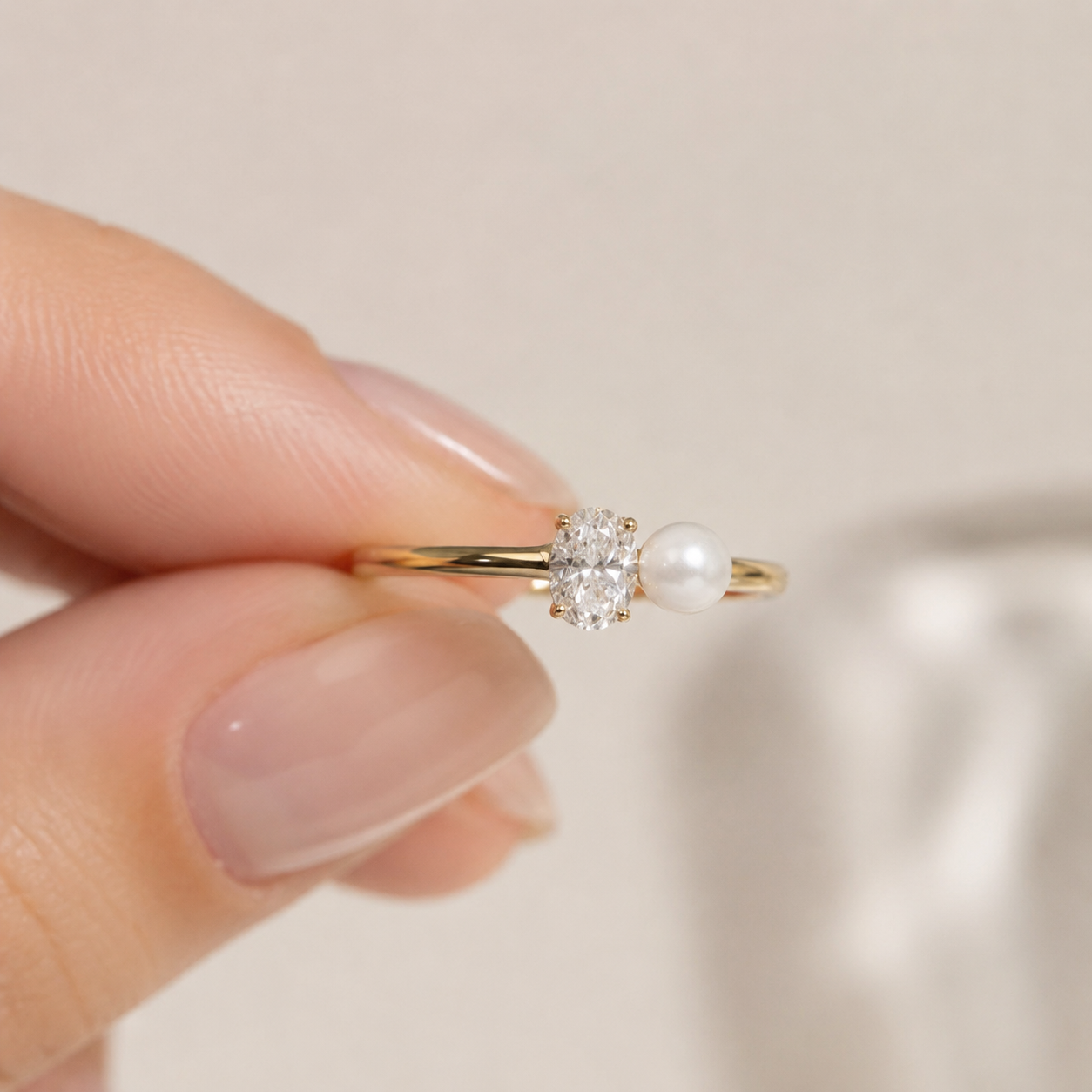 A close-up of a hand holding a delicate gold ring with a round-cut clear gemstone and a small white pearl.