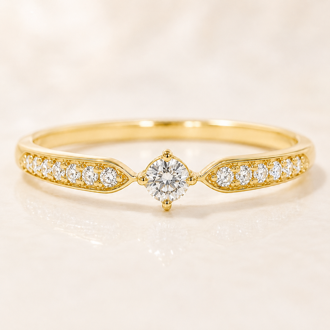 A yellow gold ring featuring a central round brilliant-cut diamond surrounded by smaller diamonds on both sides of the band, set against a soft, light beige background.