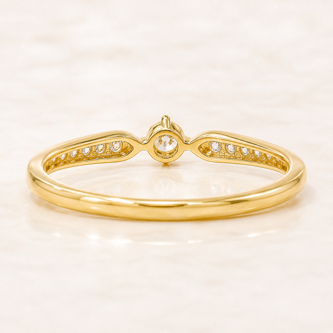A yellow gold ring with a central round-cut gemstone and small pavé-set diamonds along the band, shown on a light marble-like surface.