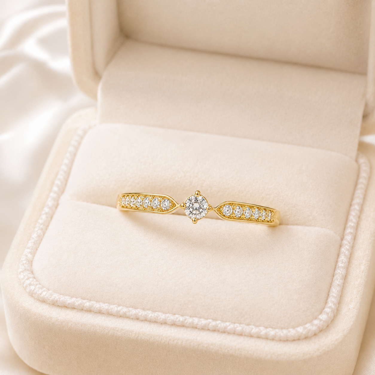 A yellow gold ring with a central round-cut diamond and pavé-set diamonds on each side, displayed in an open cream-colored velvet ring box.