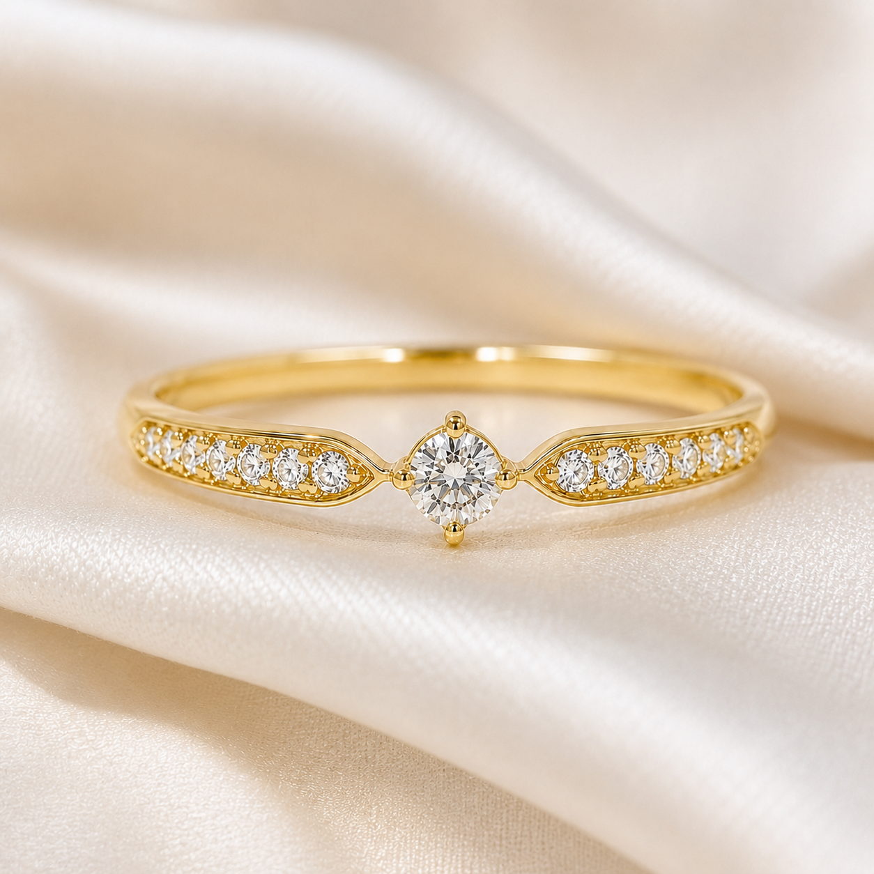 A yellow gold ring with a central round diamond and small diamonds along the shoulders, displayed on draped cream satin fabric.