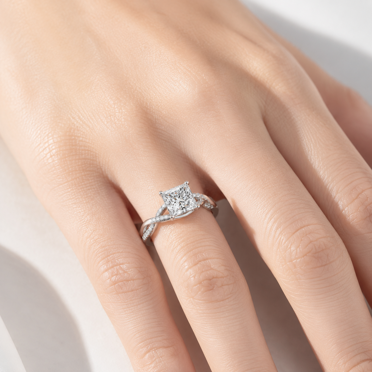 A close-up of a hand wearing a silver-toned ring with a square-cut center stone and small accent stones along the band, photographed against a soft light background.