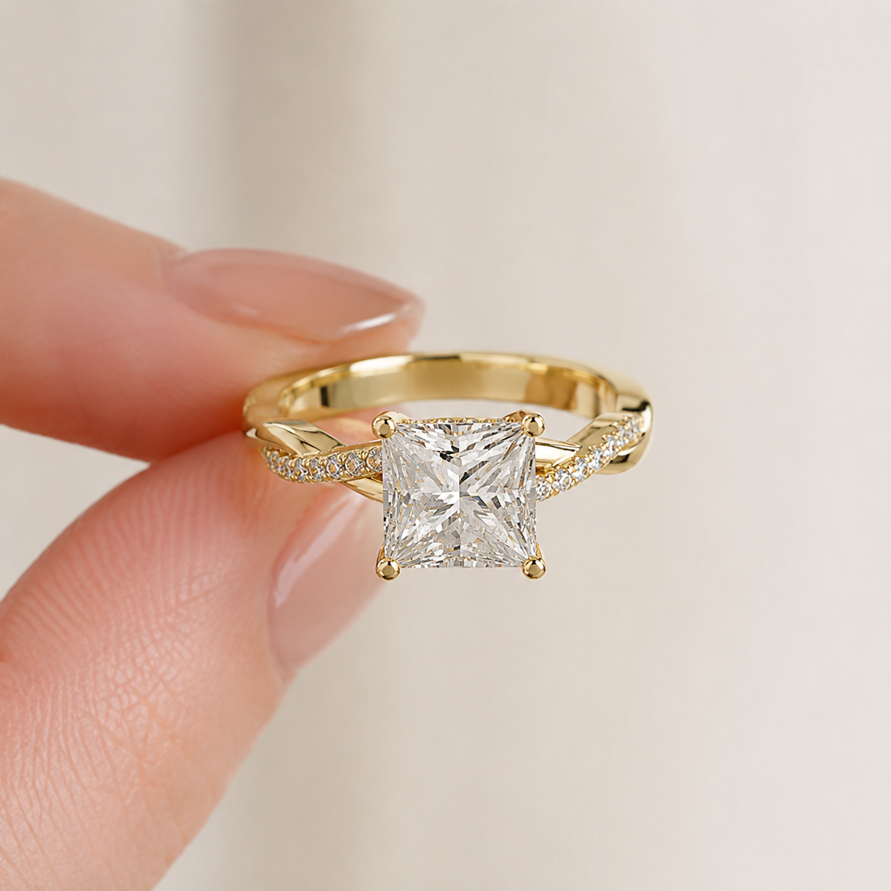 A yellow gold ring with a princess-cut clear center stone and pavé-set side stones, held between fingers against a soft light beige background.