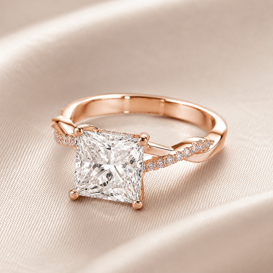 A rose gold ring featuring a large princess-cut diamond center stone and small pavé diamonds along the band, displayed on a soft beige satin fabric background.