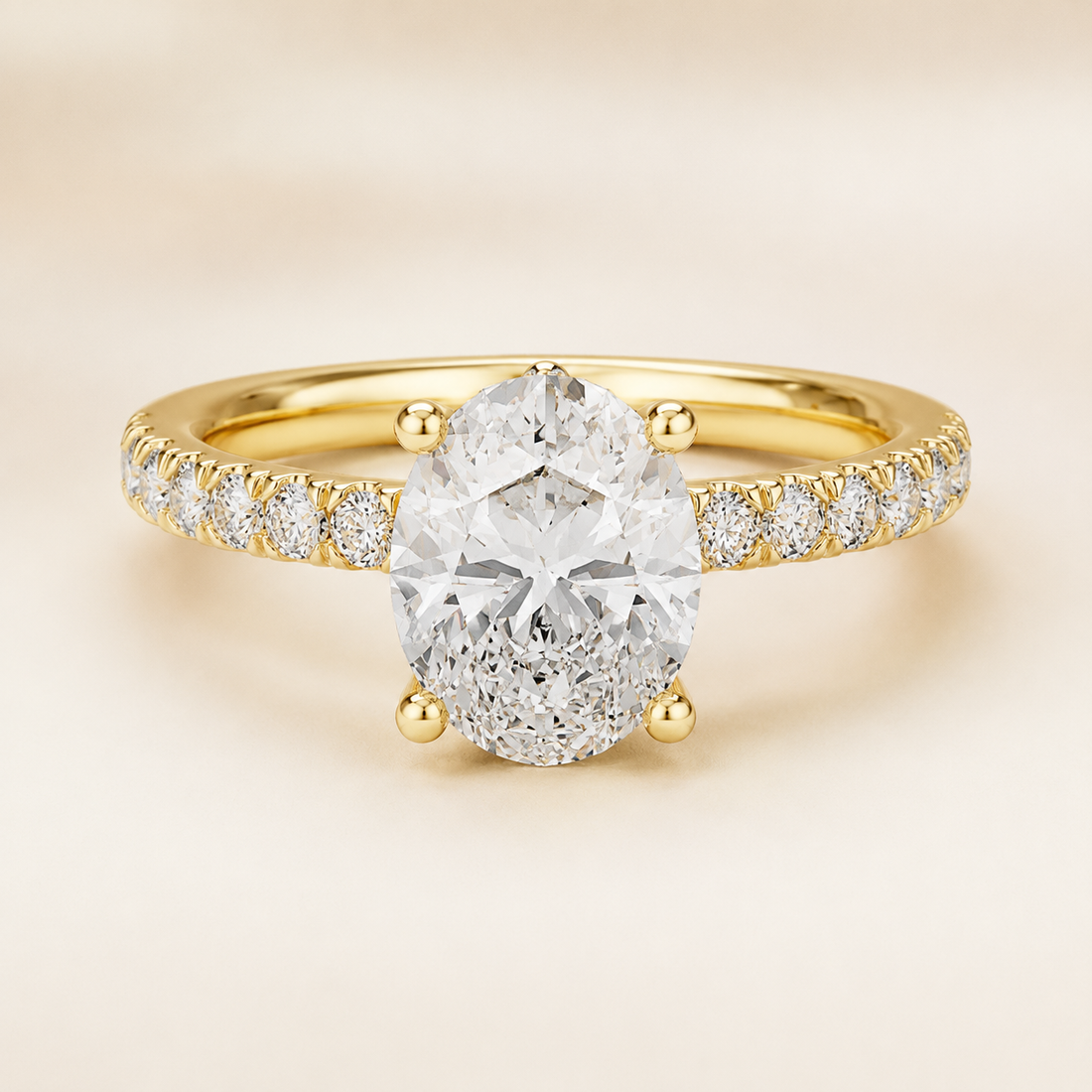 A yellow gold engagement ring featuring a large oval-cut center stone in a four-prong setting, with a pavé band set with small round diamonds, shown on a soft beige background.