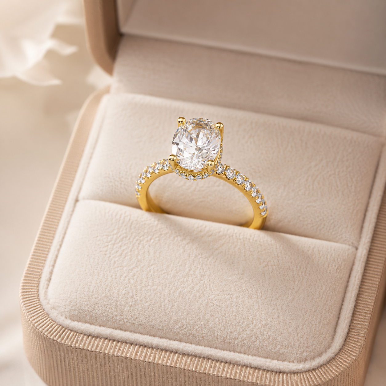 A yellow gold solitaire engagement ring with a round-cut clear center stone and small pavé-set stones on the band, displayed in an open beige jewelry box.