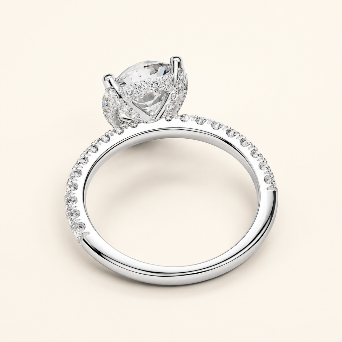 A silver-toned diamond ring with a large oval center stone and a halo of smaller diamonds, set on a slim pavé band, shown on a light cream background.
