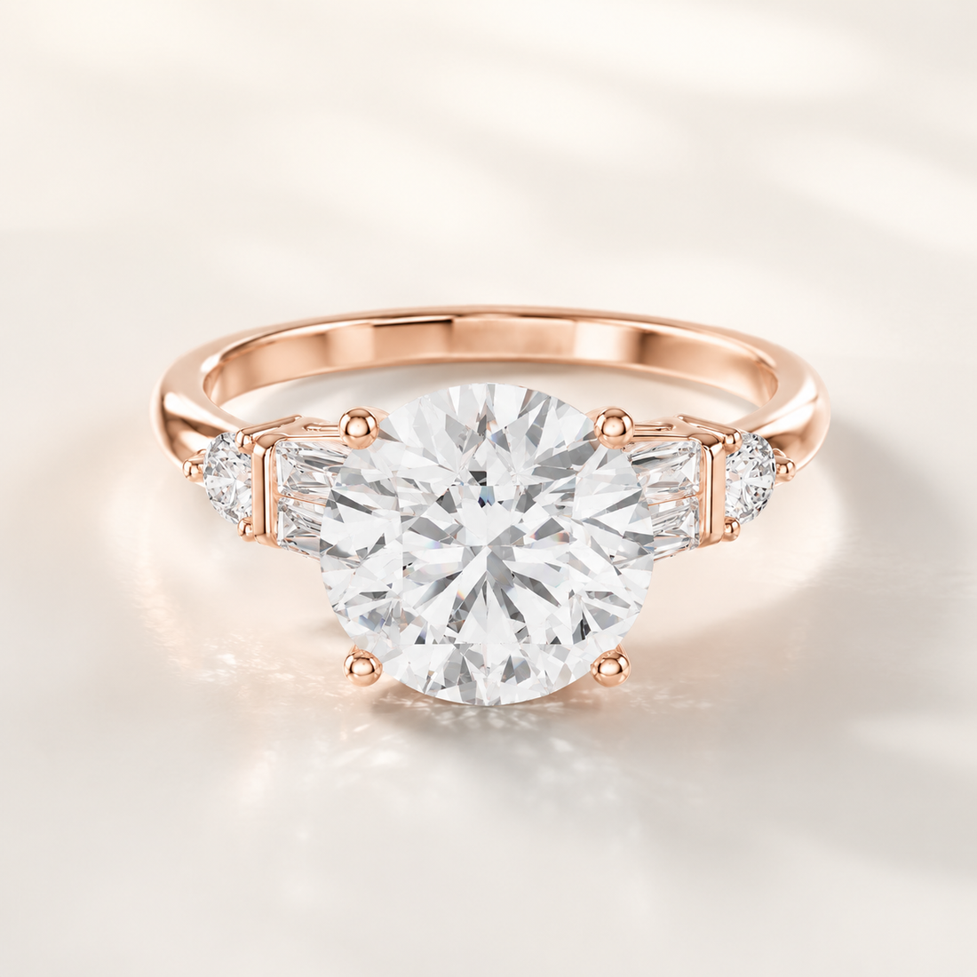 A rose gold engagement ring featuring a large round-cut center stone and smaller side stones, photographed on a soft light beige background.
