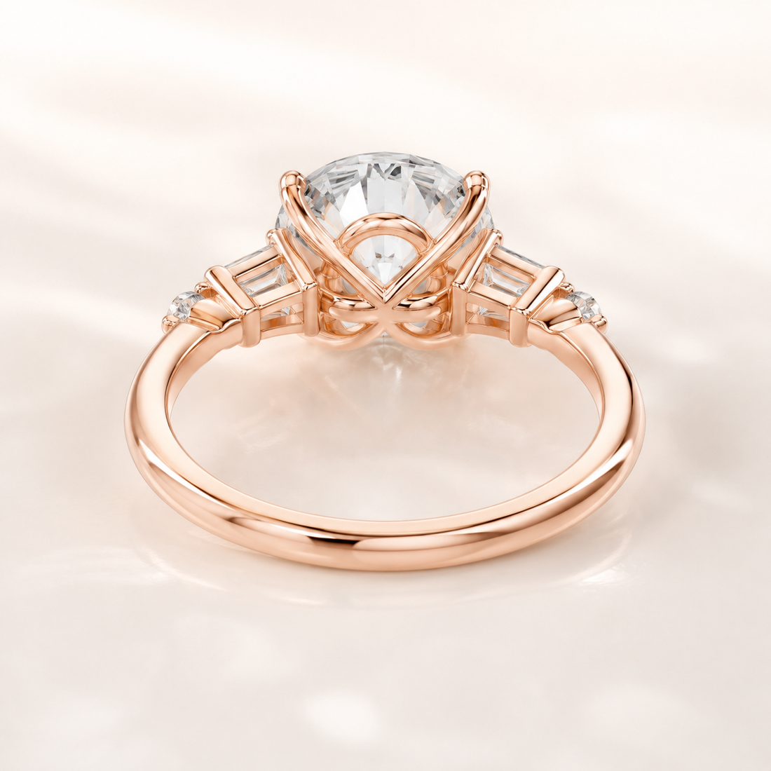 A rose gold engagement ring featuring a large round brilliant-cut center stone and baguette side stones, shown on a soft, light cream background.