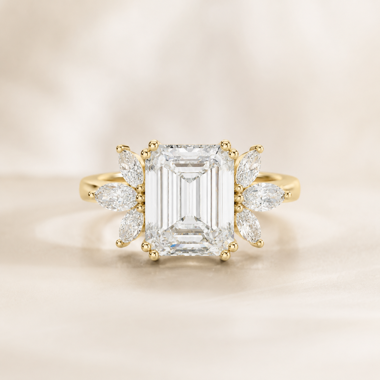 An emerald-cut diamond ring with a yellow gold setting and marquise-cut diamond accents, presented on a soft, light beige background.