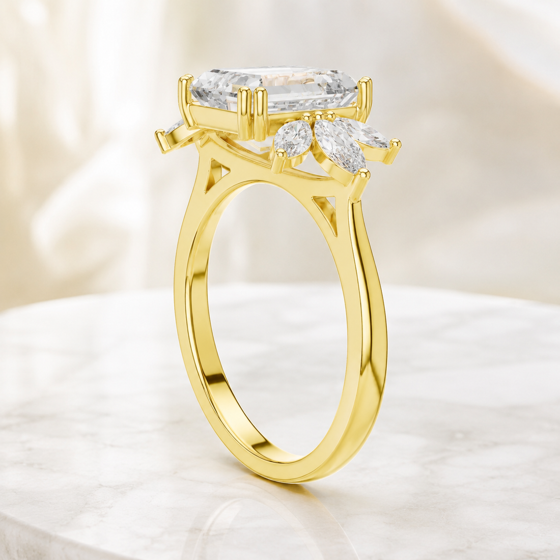 A yellow gold ring with a large rectangular clear gemstone and smaller marquise-cut stones, displayed on a light marble surface with a soft cream background.