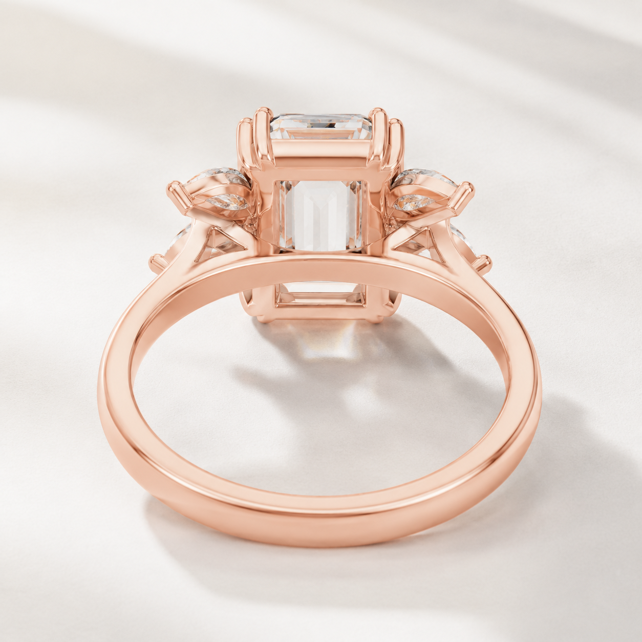 Rose gold ring with a large rectangular clear gemstone and smaller side stones, photographed on a soft light background.
