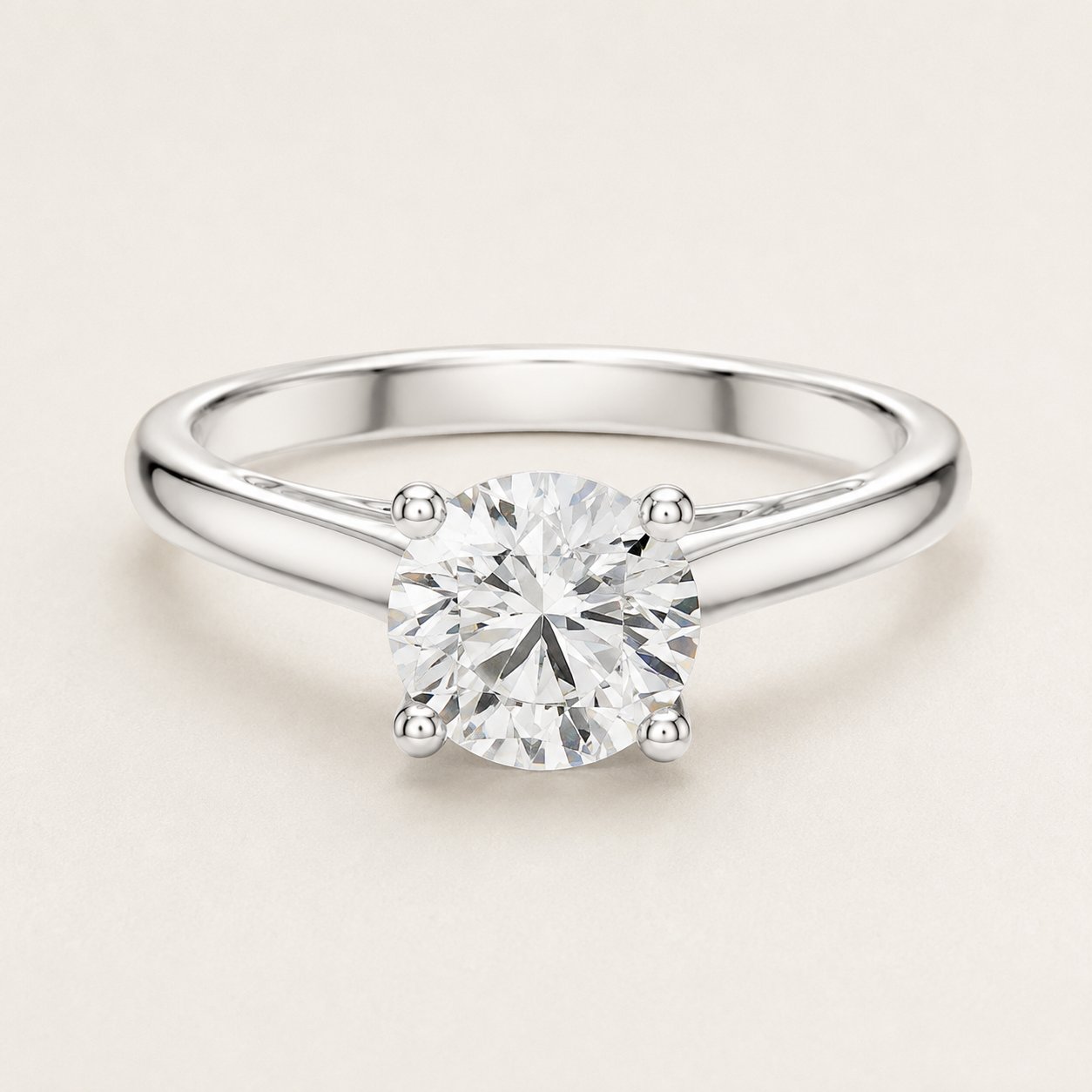 A round-cut diamond solitaire engagement ring in a polished silver-colored metal band, set against a clean, light beige background.