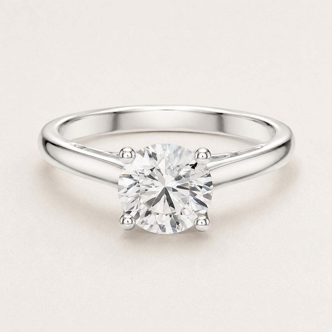 A round-cut diamond solitaire engagement ring in a polished silver-colored metal band, set against a clean, light beige background.
