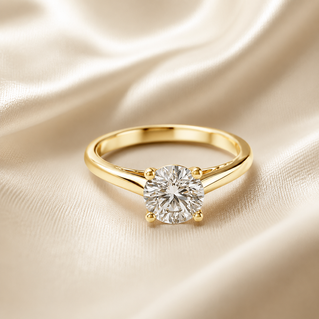 A yellow gold solitaire engagement ring with a round brilliant-cut diamond, resting on a draped cream satin fabric background.