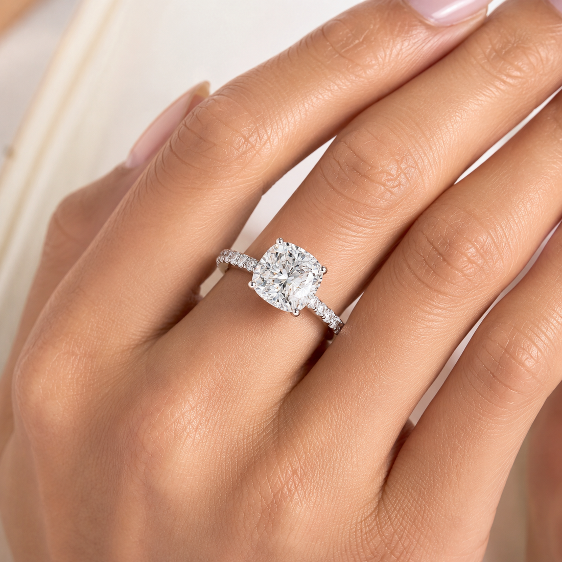 A close-up of a hand wearing a silver-toned engagement ring with a large cushion-cut diamond center stone and small pavé diamonds along the band.
