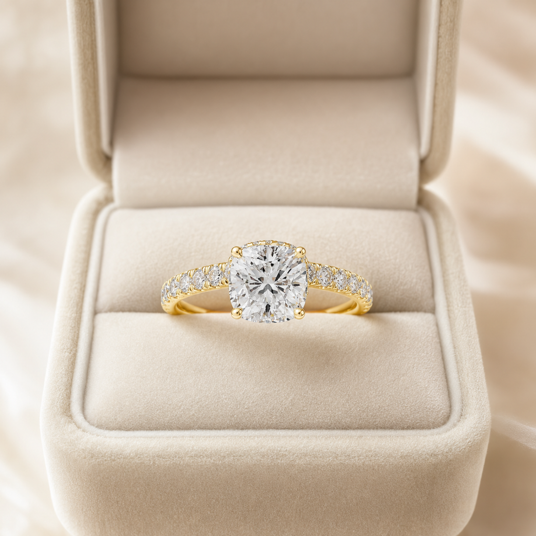 A yellow gold ring with a round-cut diamond center stone and pavé-set diamonds on the band, displayed in an open cream-colored velvet ring box.