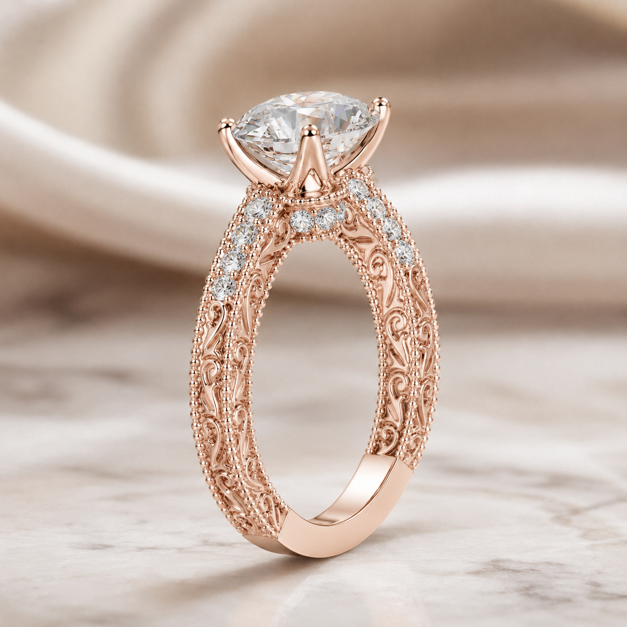 Rose gold filigree engagement ring with a marquise-cut clear center stone and small accent stones, photographed on a soft beige satin and marble surface.