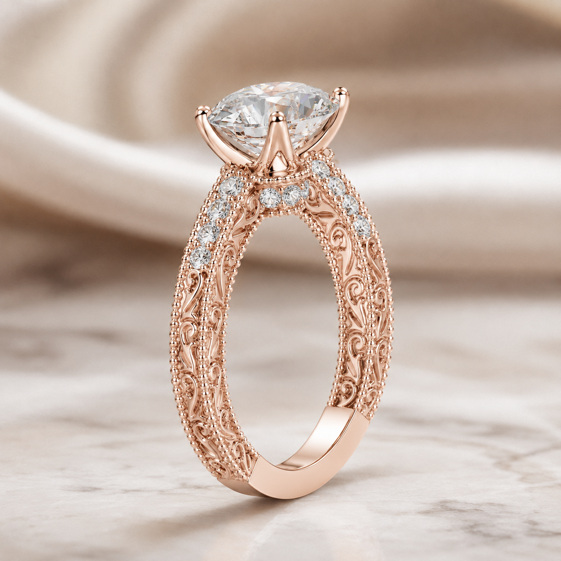 Rose gold filigree engagement ring with a marquise-cut clear center stone and small accent stones, photographed on a soft beige satin and marble surface.