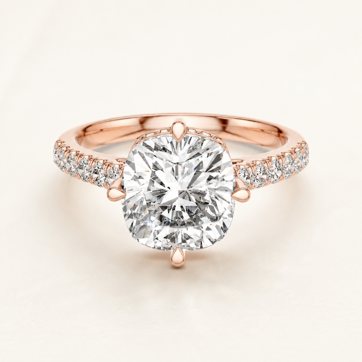 A rose gold engagement ring featuring a large cushion-cut diamond center stone in a prong setting, with pavé diamonds along the shoulders of the band, set against a clean off-white background.