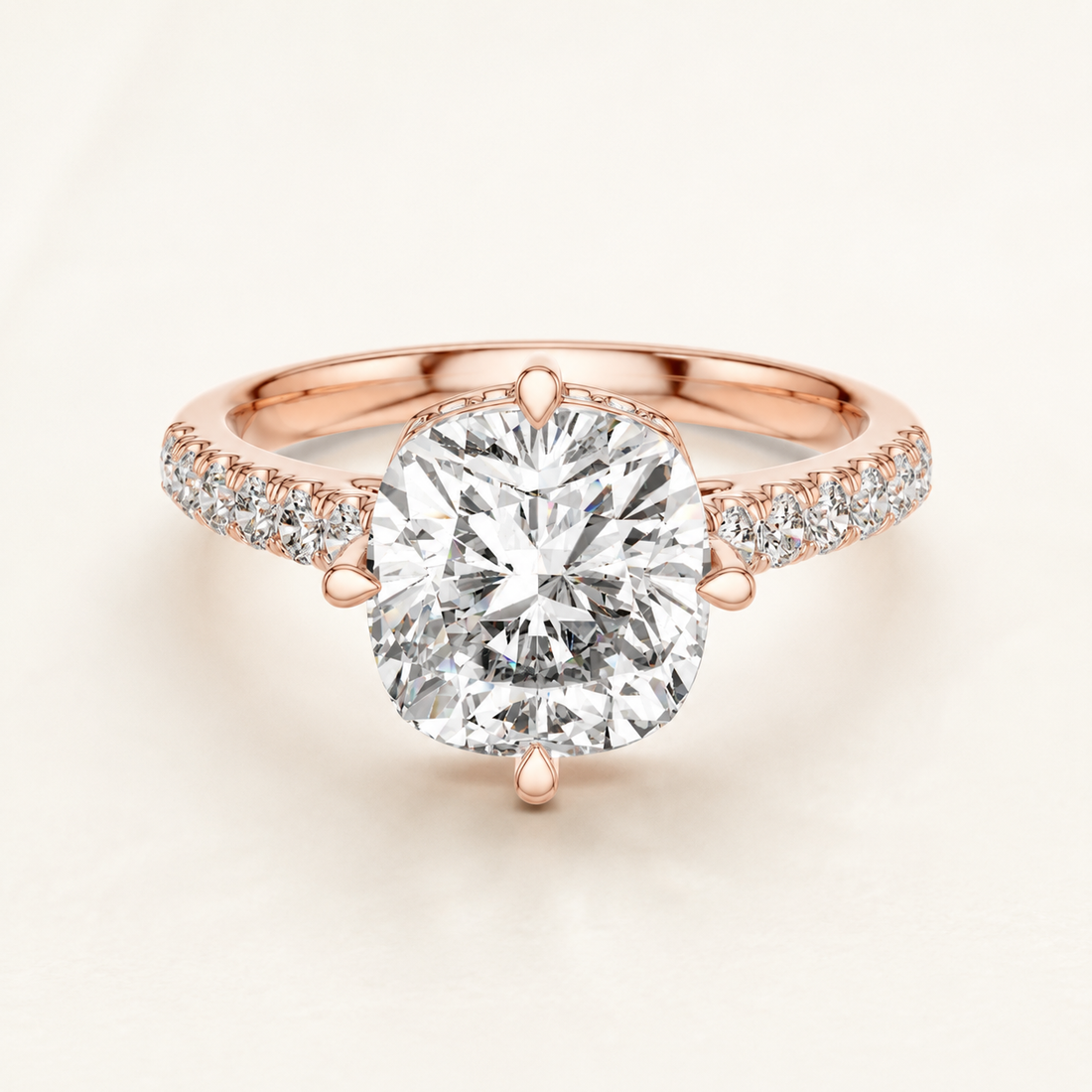 A rose gold engagement ring featuring a large cushion-cut diamond center stone in a prong setting, with pavé diamonds along the shoulders of the band, set against a clean off-white background.