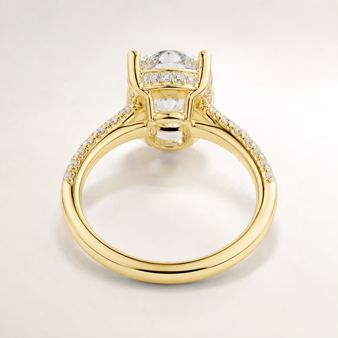 A yellow gold ring with a large round clear gemstone in a prong setting, accented by small pavé diamonds along the shoulders, shown on a light gray background.