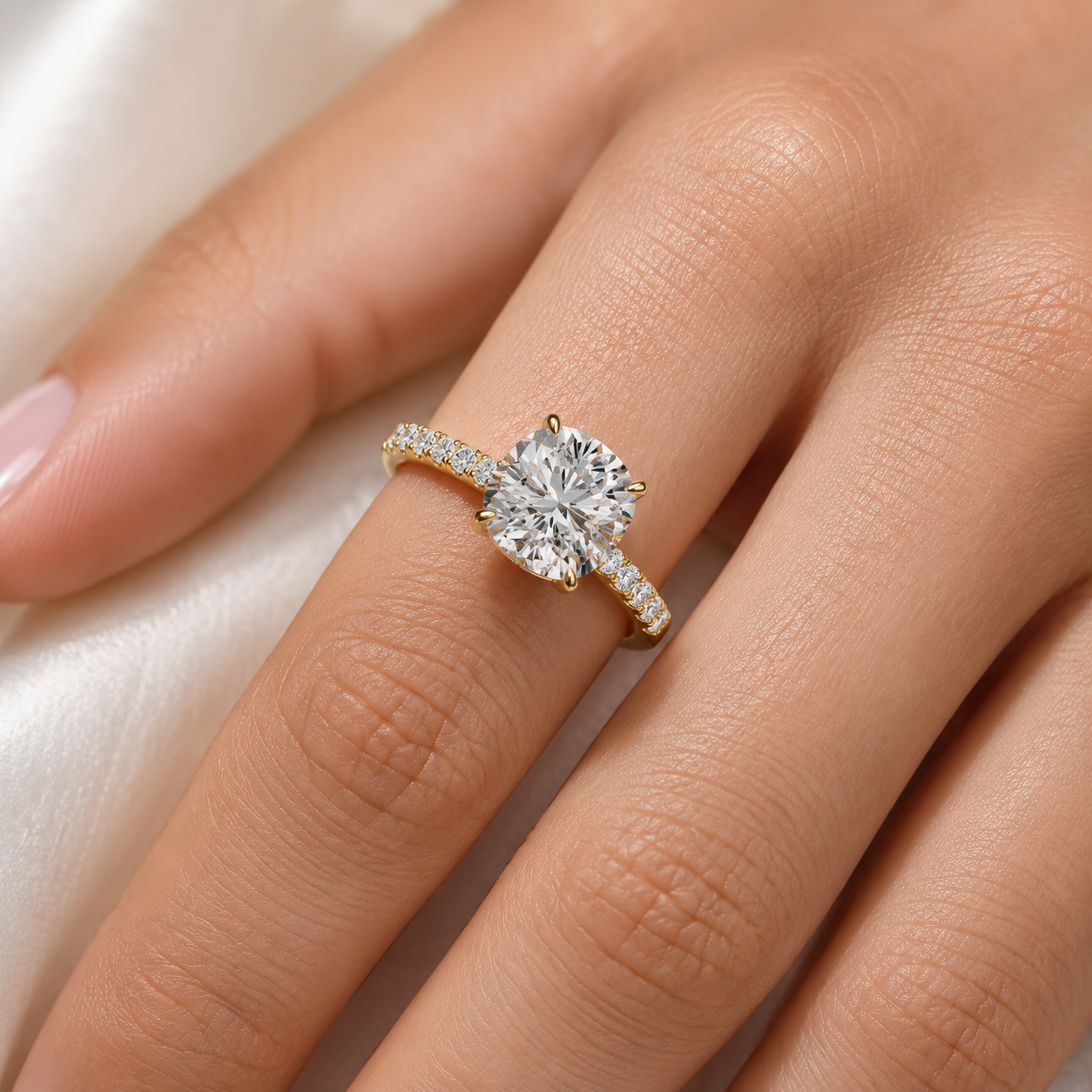 A close-up of a hand wearing a yellow gold ring with a large round-cut clear center stone and smaller stones along the band, set against a soft white fabric background.