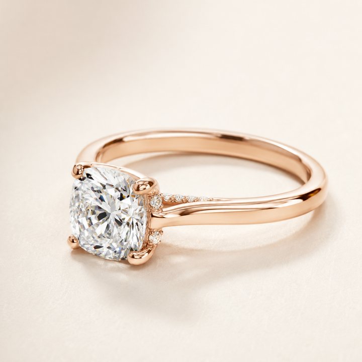 A rose gold engagement ring featuring a cushion-cut diamond solitaire and small accent diamonds on the band, set against a warm cream background.