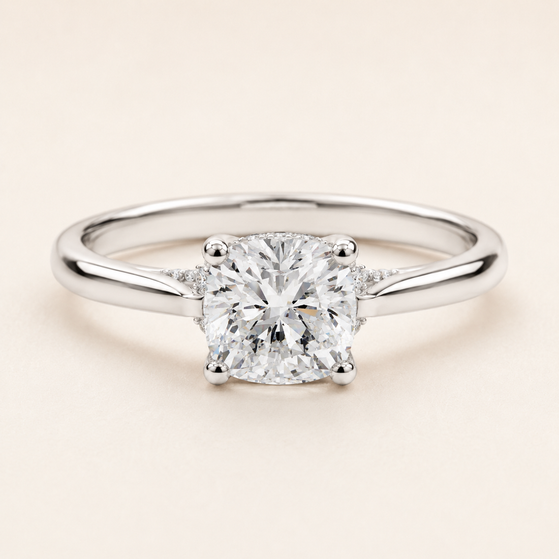 A classic solitaire engagement ring featuring a round brilliant-cut diamond set in a polished silver-colored metal band, photographed on a clean, solid light beige background.