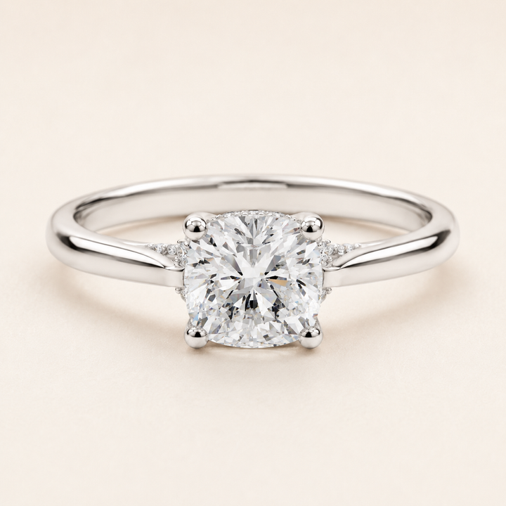 A classic solitaire engagement ring featuring a round brilliant-cut diamond set in a polished silver-colored metal band, photographed on a clean, solid light beige background.