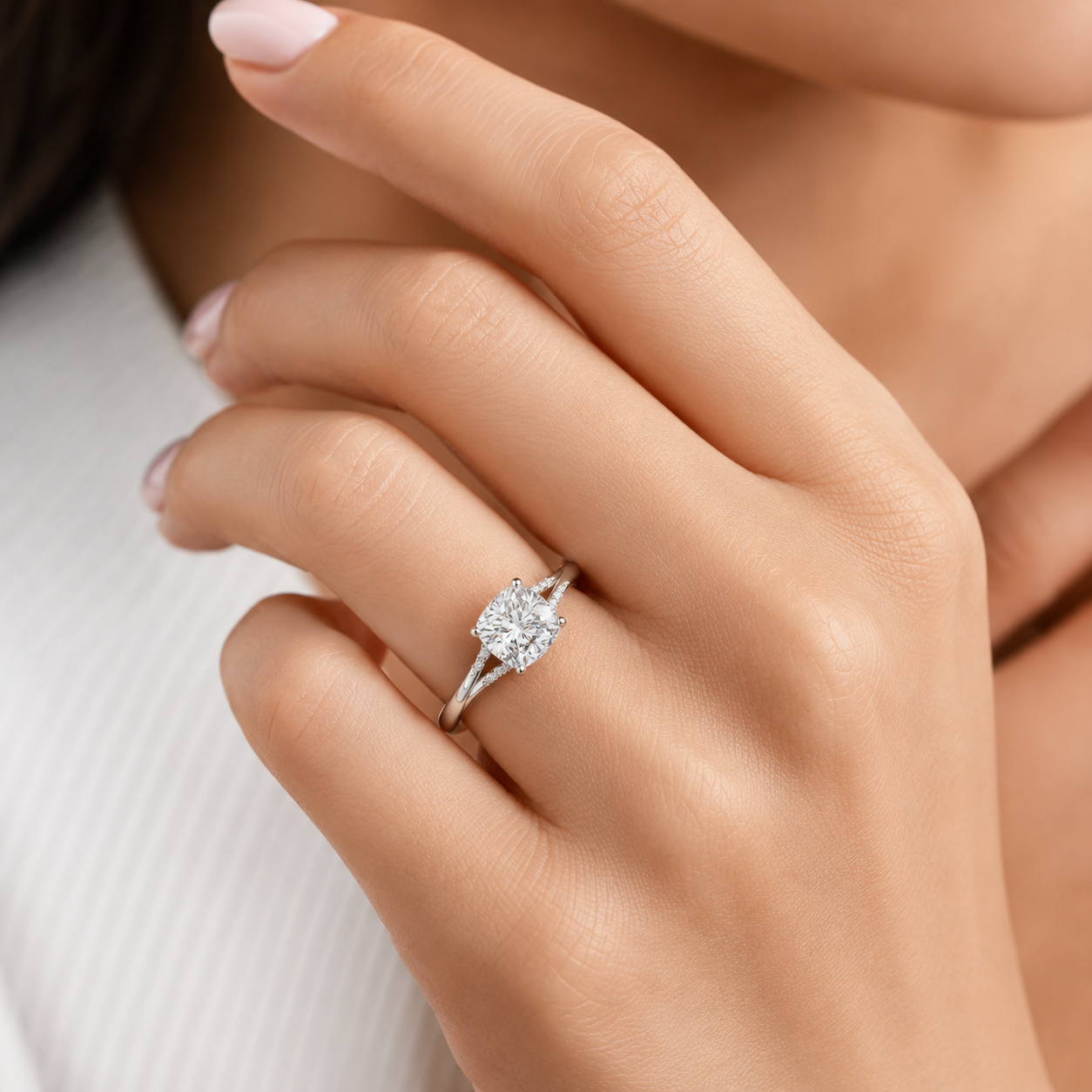 A close-up of a woman's hand wearing a silver-toned ring with a round brilliant-cut diamond. The ring is shown on the ring finger against a soft, light-colored background.
