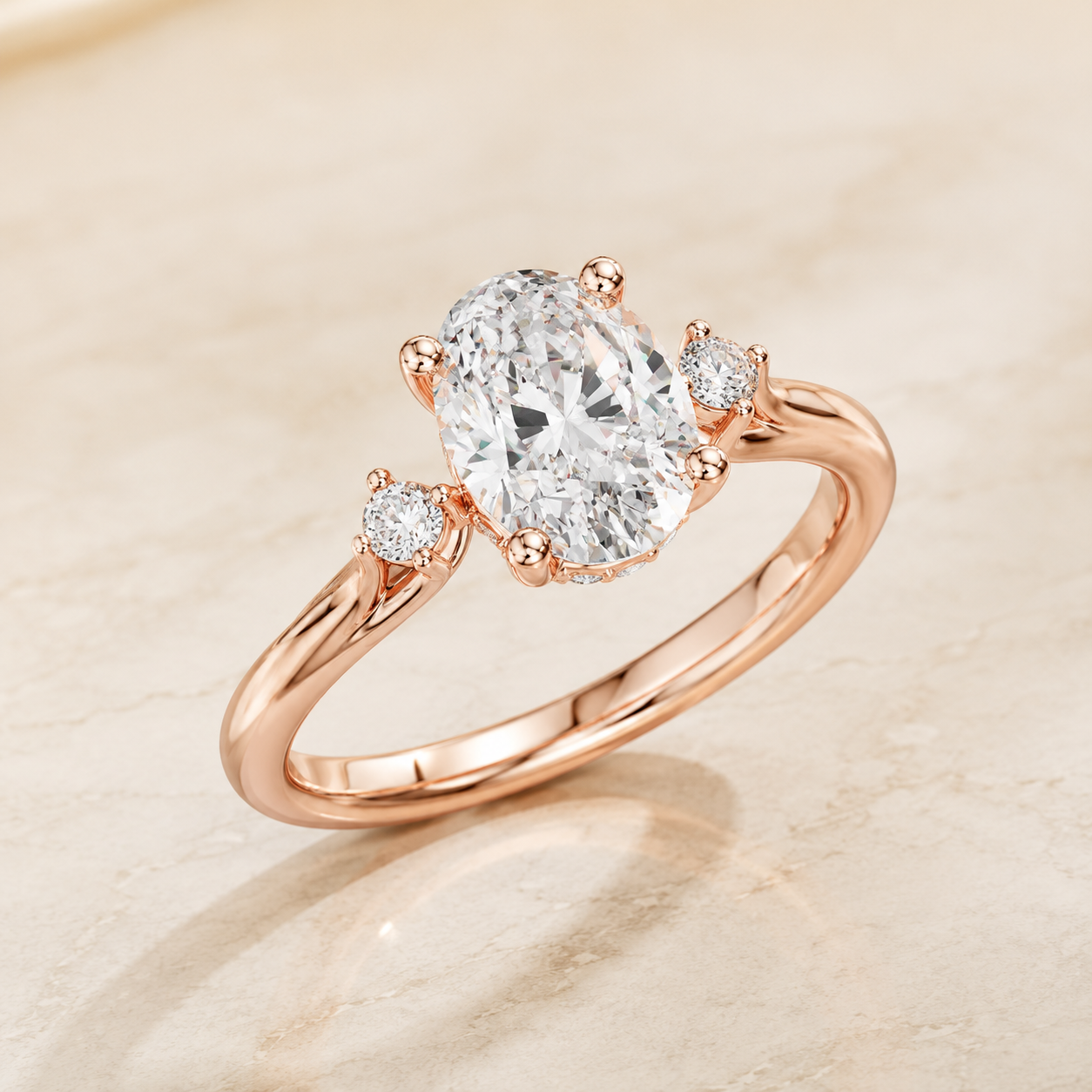 Rose gold engagement ring with an oval-cut center diamond and two round side diamonds, set on a warm beige marble surface.