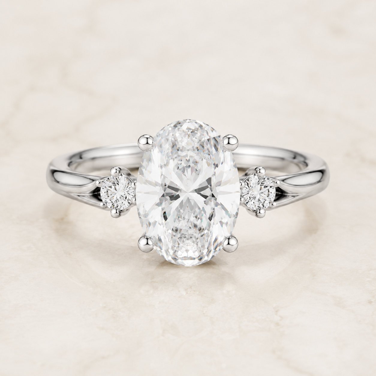An oval diamond engagement ring with a silver-colored band and two small round diamonds on either side, set against a light marble background.