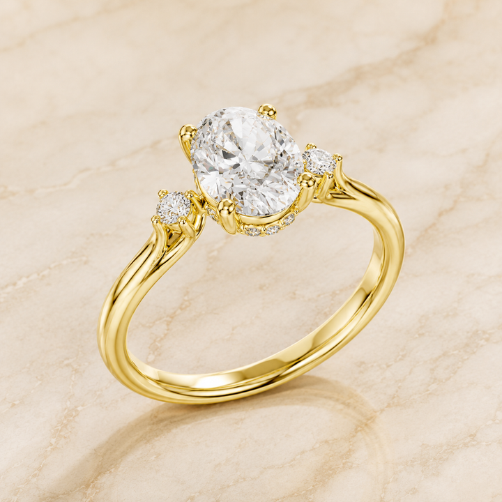 A yellow gold solitaire ring with a round-cut center stone and two smaller accent stones, displayed on a light beige marble surface.