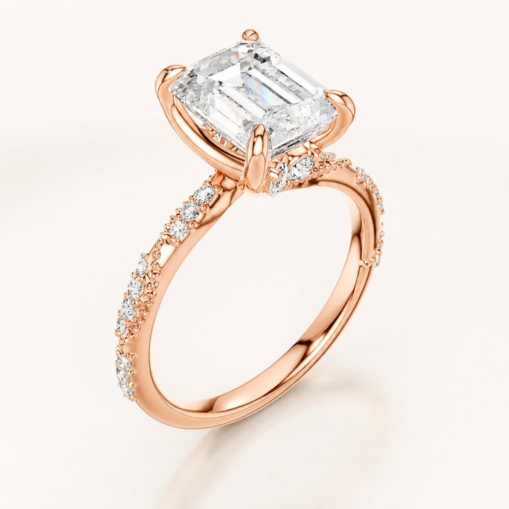 A rose gold engagement ring featuring a large emerald-cut diamond center stone and pavé diamonds along the shank, set against a clean off-white background.