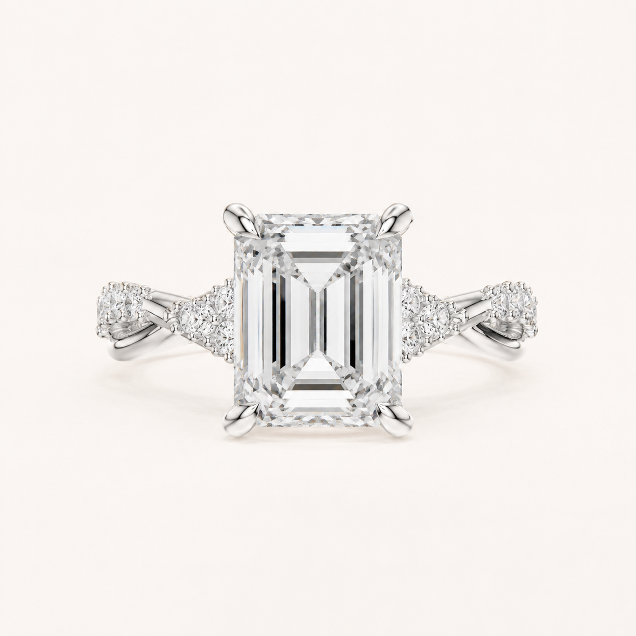 An emerald-cut diamond engagement ring in a silver-toned setting with pavé accents on the shoulders, centered on a light cream background.