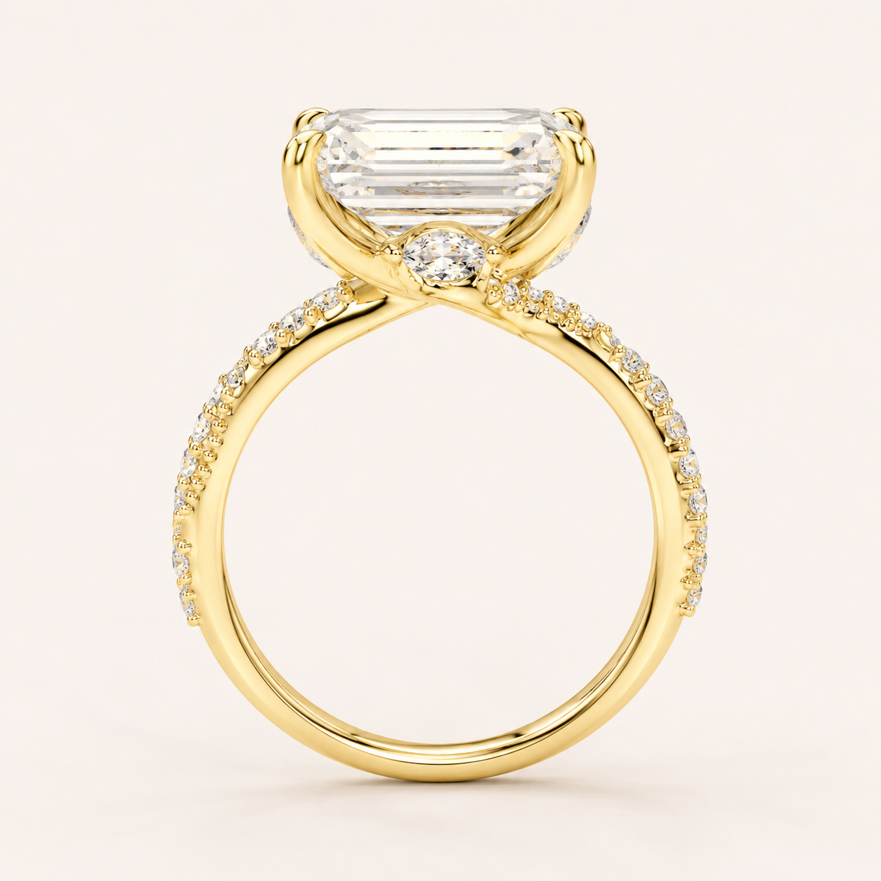 A yellow gold ring featuring a large rectangular baguette-cut clear center stone and a small round clear accent stone, with pavé-set clear stones along the shank, shown on a light cream background.