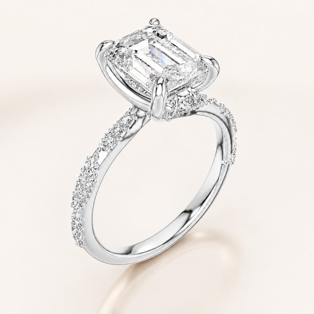 An emerald-cut diamond ring in a polished white gold or platinum setting, featuring a pavé band and small accent diamonds, shown on a light cream background.