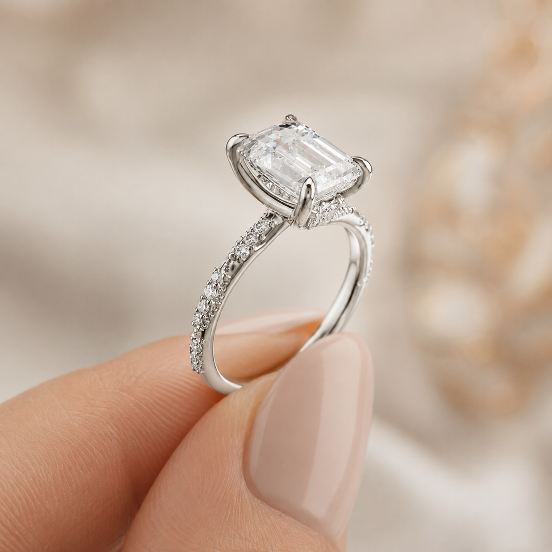 A silver engagement ring with a large rectangular emerald-cut diamond and pavé-set band, held between fingers against a soft beige background.