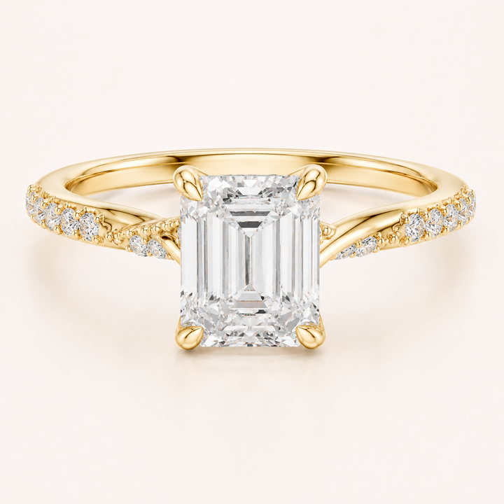 An emerald-cut diamond engagement ring in yellow gold, featuring a large central diamond and smaller diamonds set along the shoulders of a polished band, shown on a light cream background.