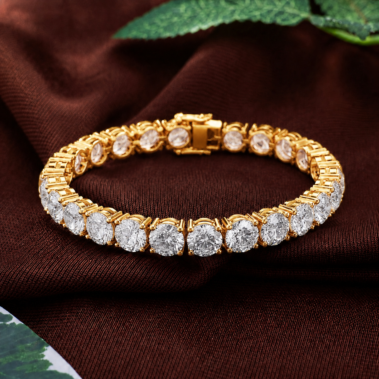 A gold tennis bracelet with round-cut clear gemstones, displayed on a dark brown textured fabric background with green leaves in the corner.