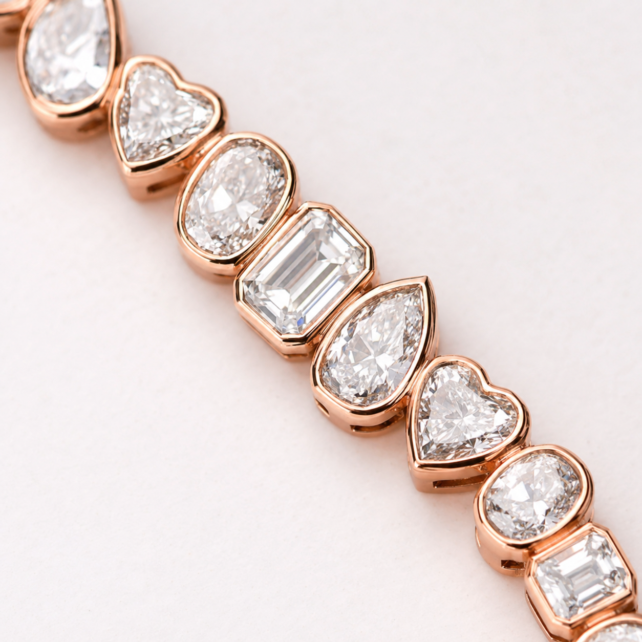 A close-up of a rose gold bracelet featuring alternating heart and oval-cut clear gemstones in polished rose gold settings, set against a clean white background.