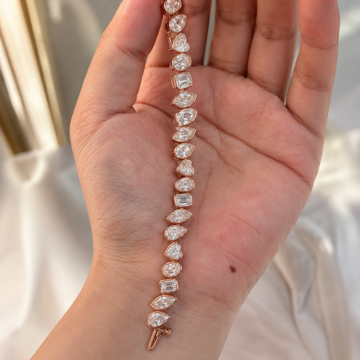 A close-up of a hand holding a rose gold bracelet adorned with clear marquise and baguette-cut gemstones.