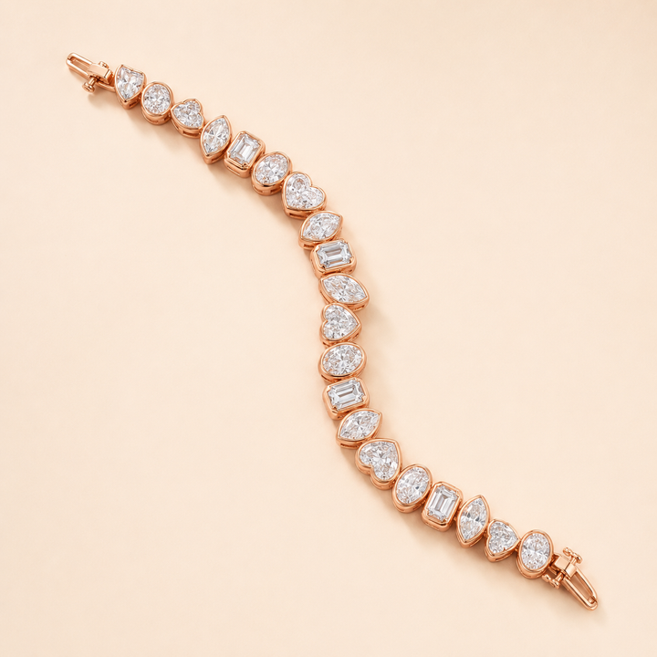 A rose gold tennis bracelet featuring a curved line of heart-shaped and baguette-cut clear gemstones, displayed on a solid pale peach background.