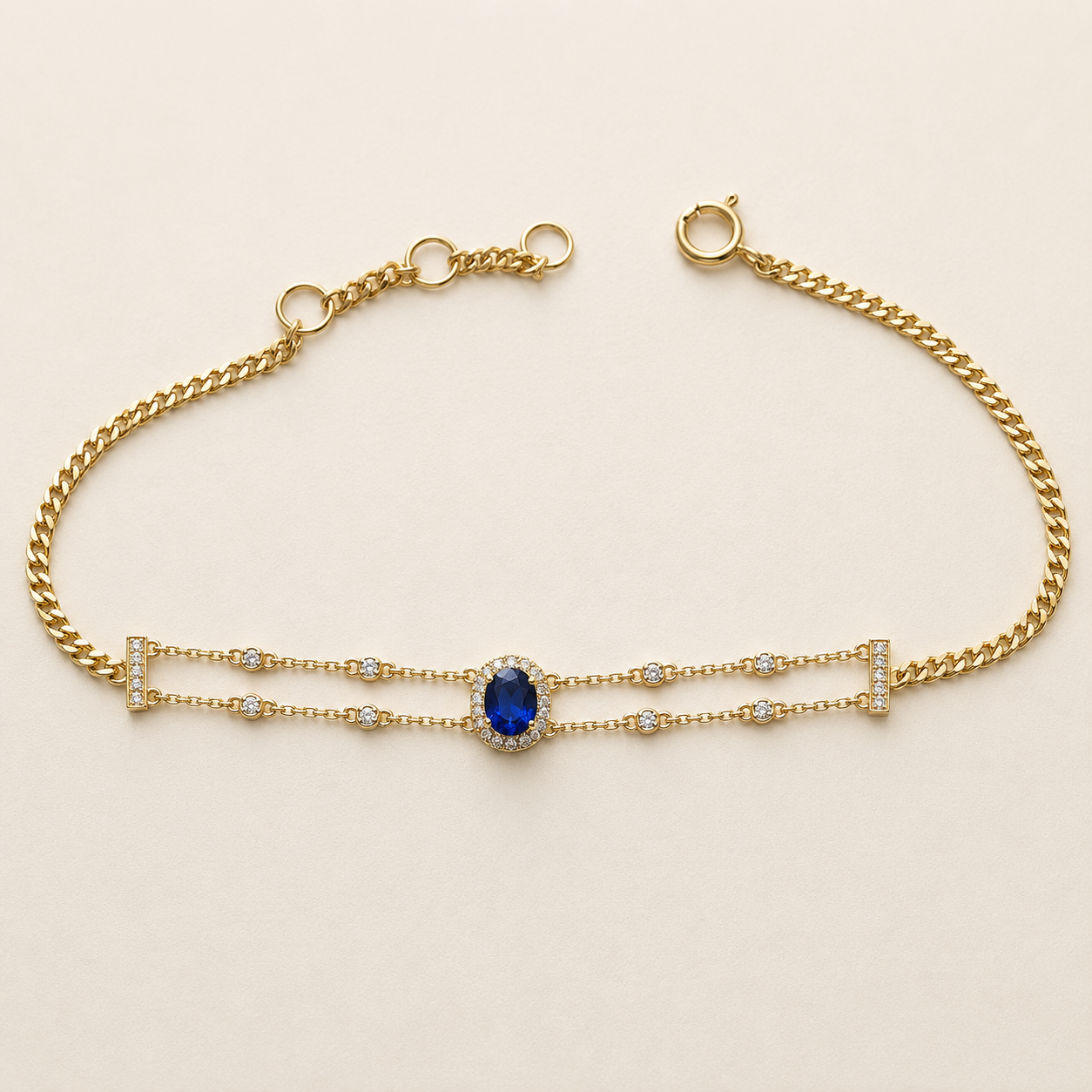 A gold chain bracelet featuring a central oval blue gemstone surrounded by small clear stones, with delicate gold links extending from the sides, photographed on a light beige background.