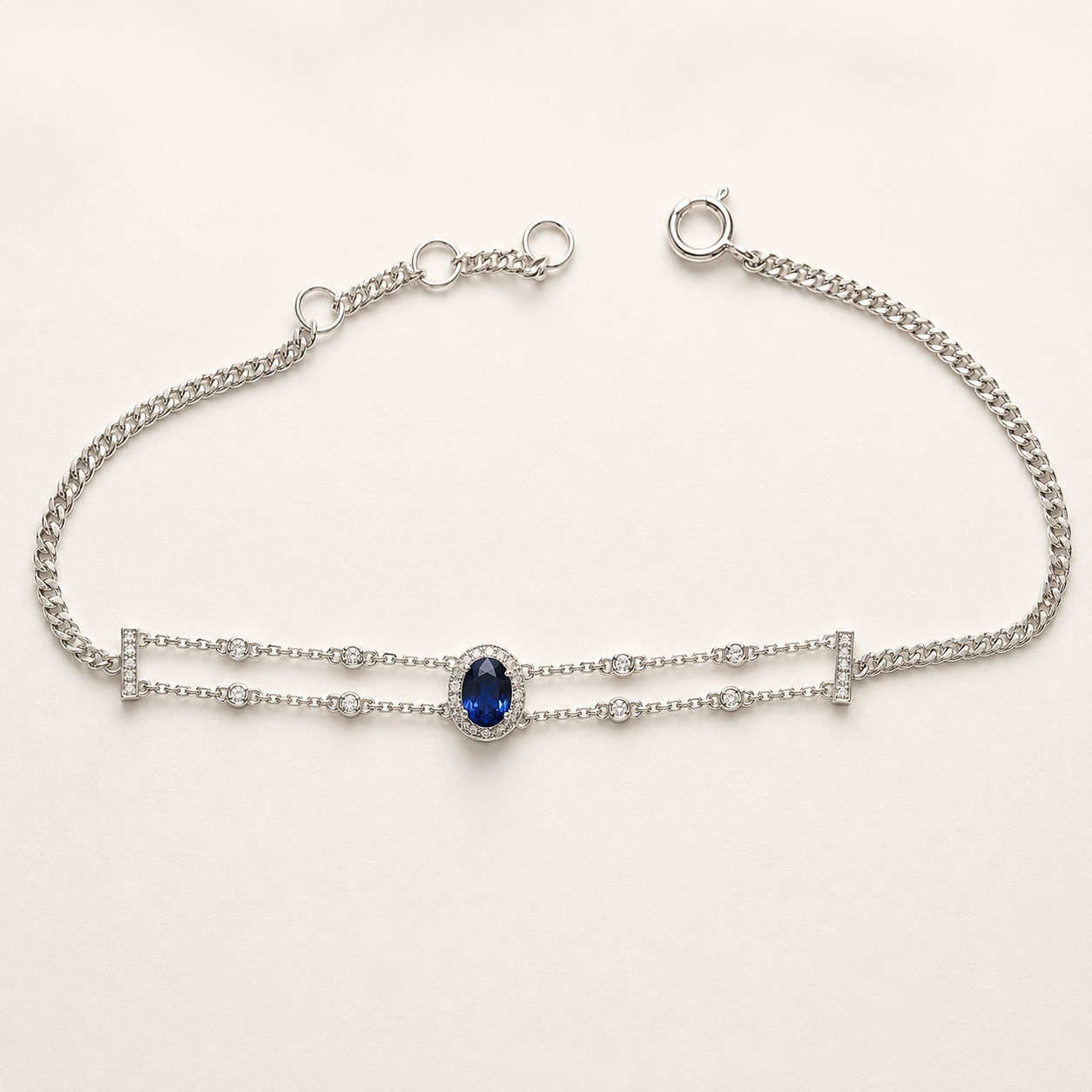 A silver double-strand chain bracelet featuring a central oval-cut deep blue gemstone surrounded by small clear stones, displayed on a clean white background.