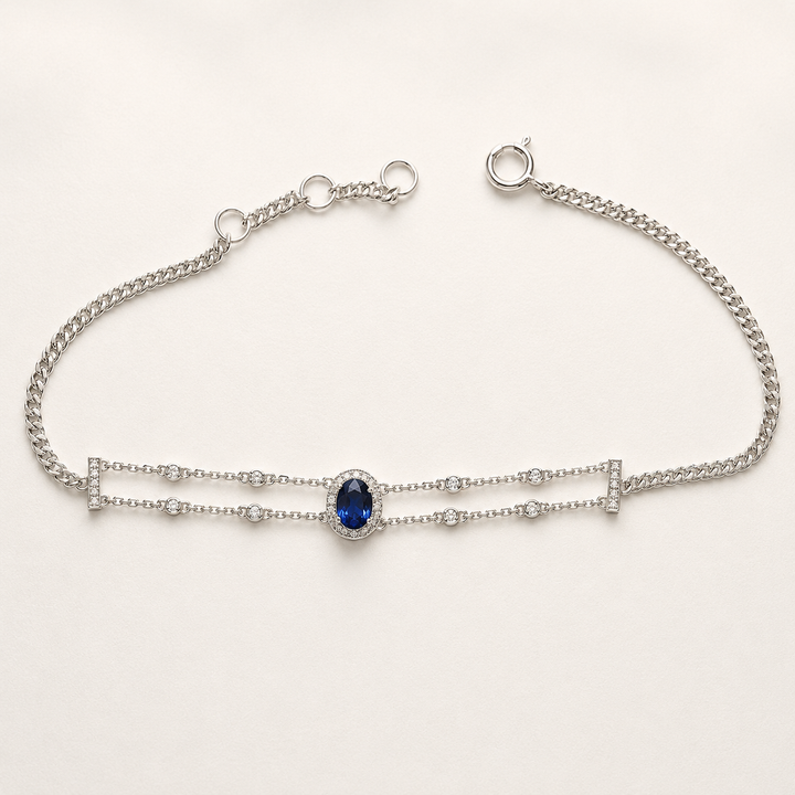 A silver double-strand chain bracelet featuring a central oval-cut deep blue gemstone surrounded by small clear stones, displayed on a clean white background.