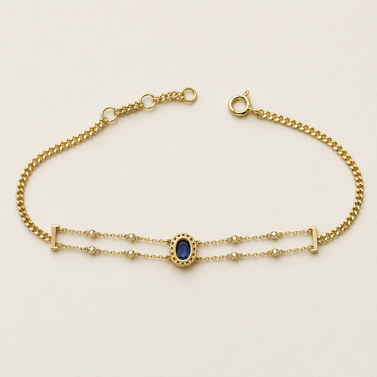A gold chain bracelet featuring a central oval blue gemstone surrounded by a beaded gold border, with double parallel chains and small bead accents.